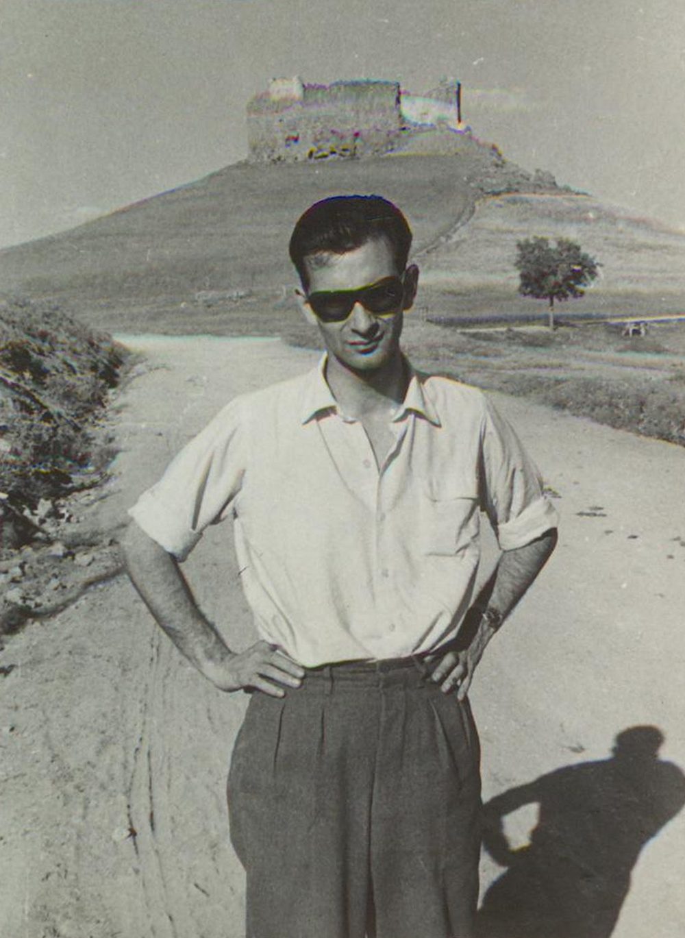 Jesús Fernández Santos, de pie en un camino, con gafas de sol y las manos en la cintura; al fondo, un castillo sobre una colina.